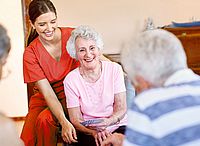 Senioren sitzend spielend und lachend am Tisch mit Pflegerin