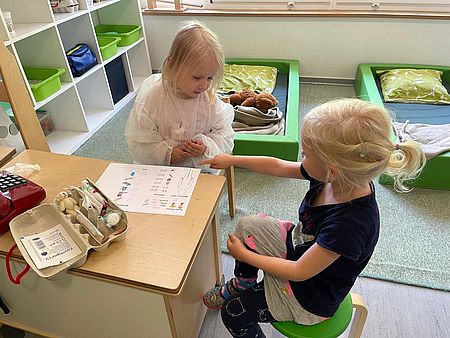Kita-Kind im Arztkittel verkleidet spricht mit anderem Kind