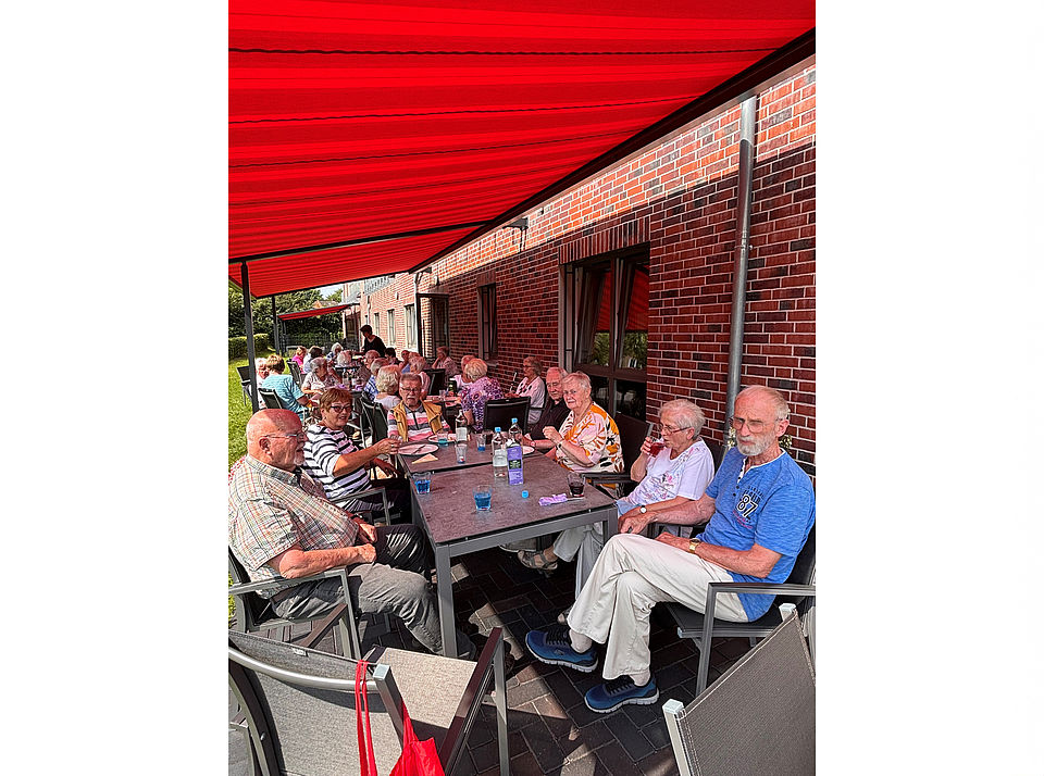 Seniorentreff Eine große Gruppe Senioren sitzt fröhlich an Tischen auf der Terrasse unter der Markiese