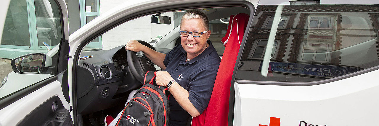 Mitarbeiterin der Ambulante Pflege lächelt aus dem DRK Dienstwagen