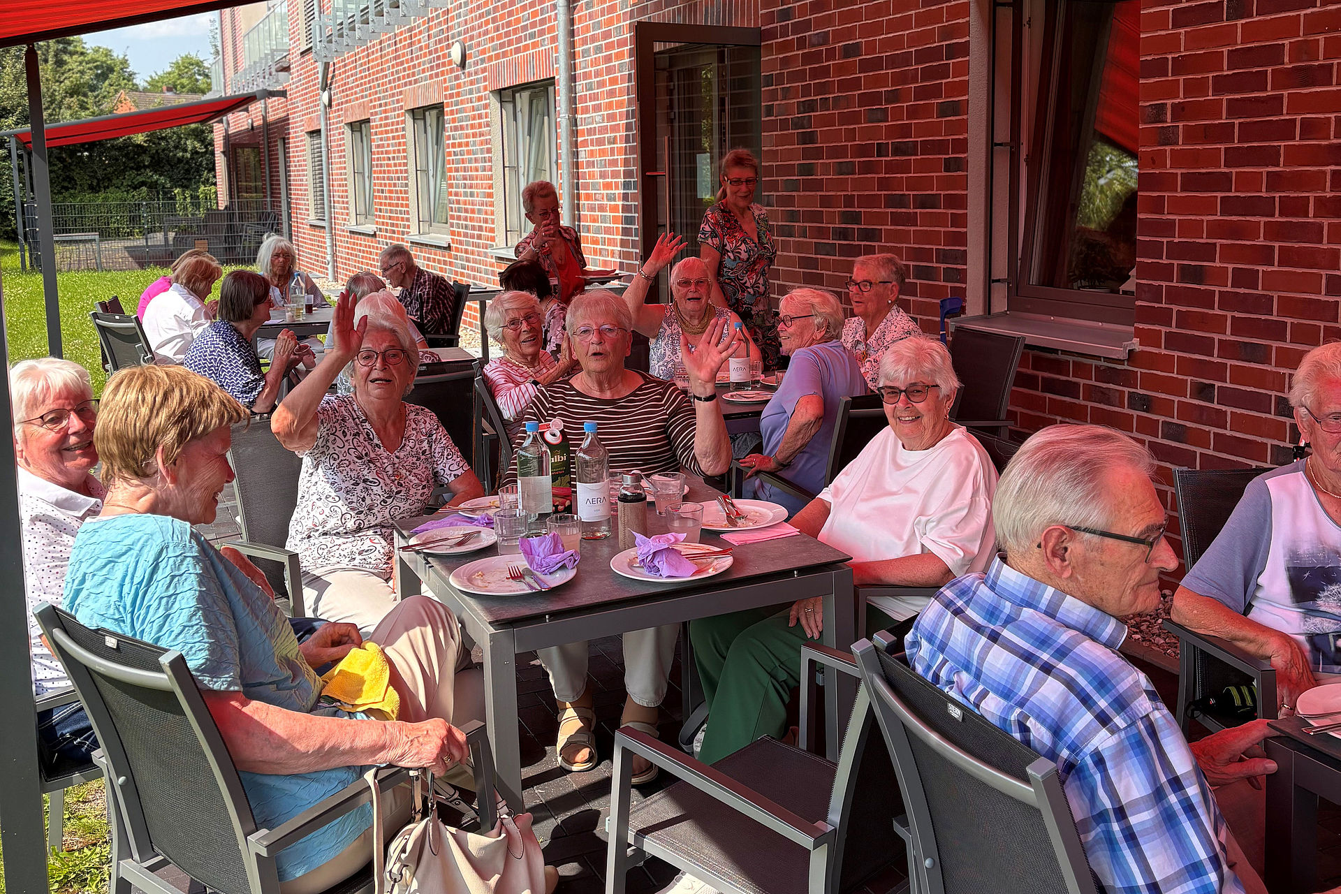 Grillen Titel Eine fröhliche Gruppe SeniorInnen sitzt an Tischen auf der Terrasse unter der Markiese