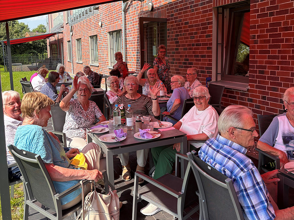Grillen Titel Eine fröhliche Gruppe SeniorInnen sitzt an Tischen auf der Terrasse unter der Markiese