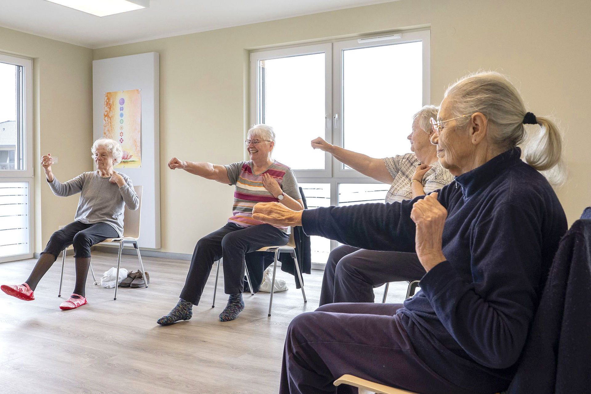 Eine Gruppe von Seniorinnen sitzt im Kreis auf Stühlen und macht Gymnastik