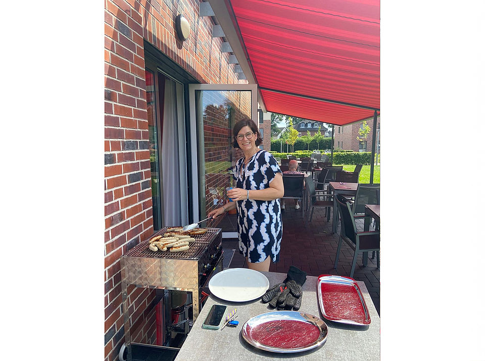 Grillen Bergzog Dorit Bergzog steht lächelnd am Grill und brät Würstchen